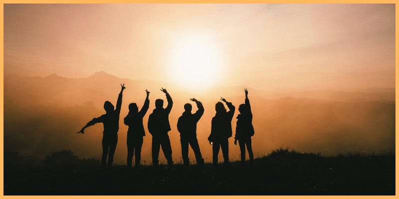 Silhouette of a group of people standing in front of a sunset