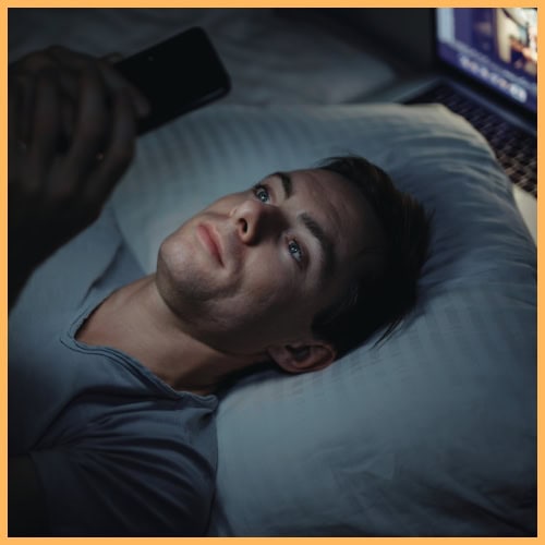 Man laying bed starting at the phone with laptop beside. completly focused on the phone